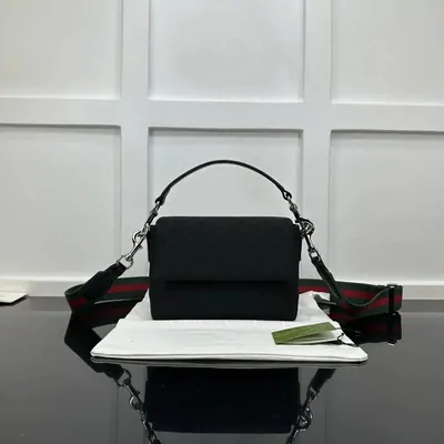 A structured black top-handle handbag standing on a pale box in a plain room