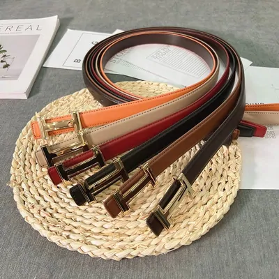 Four slim leather belts with gold buckles coiled on a woven straw mat